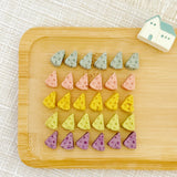 Tiny swiss-cheese wedge shaped chicken cookies in gray, pink, yellow, green and purple on a white plate