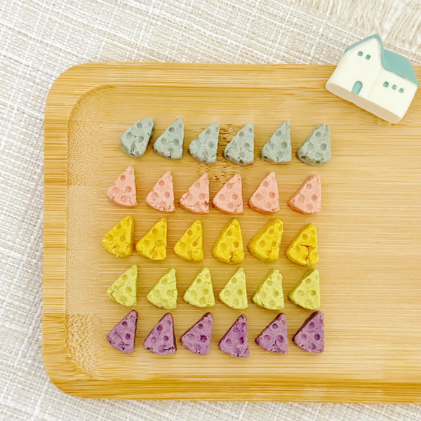 Tiny swiss-cheese wedge shaped chicken cookies in gray, pink, yellow, green and purple on a white plate