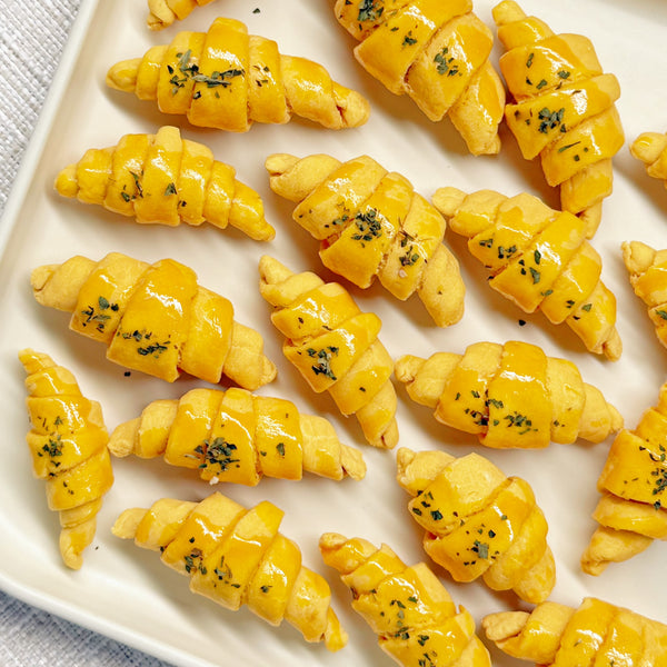 Golden mini croissant-shaped chicken bites with a parsley sprinkle on a white plate