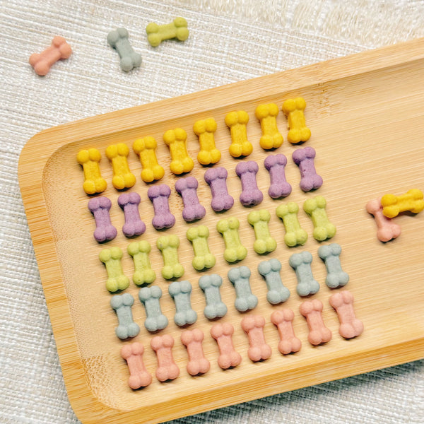 Extra-mini rainbow bone-shaped chicken cookies in yellow, purple, green, blue and pink on a white plate